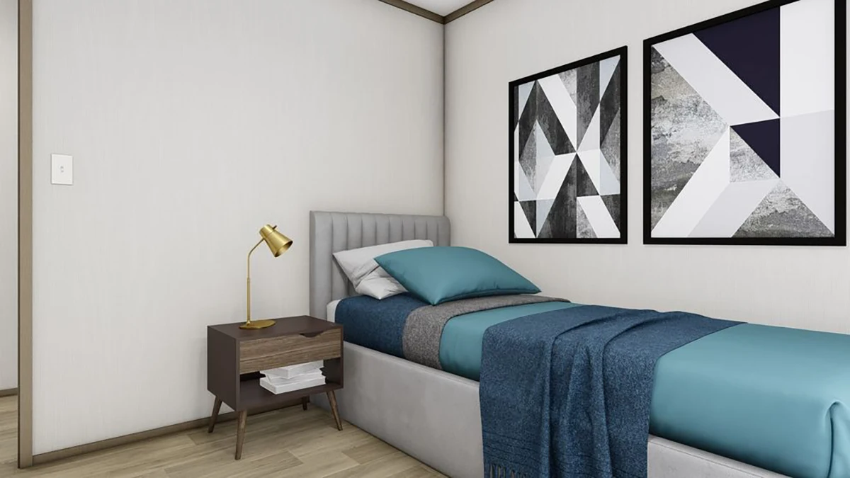 A neatly made single bed with blue and gray bedding, next to a wooden nightstand with a gold lamp, and two abstract art pieces on the wall.