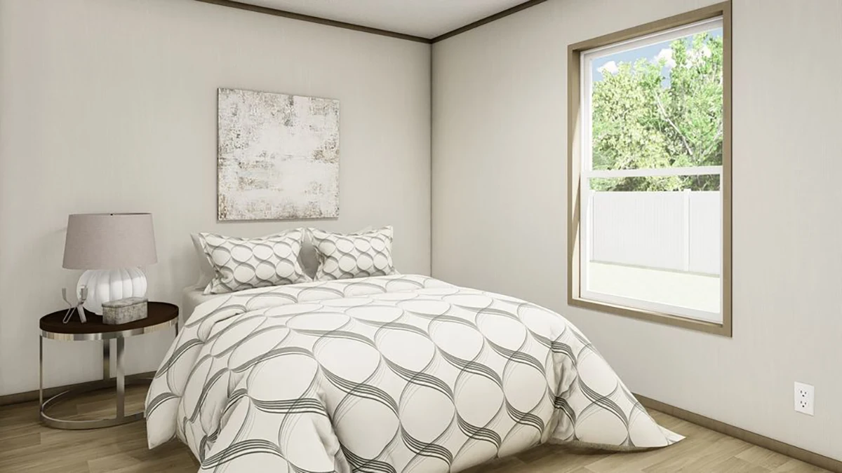 A bedroom with a double bed, patterned bedding, a round side table with a lamp, a window with outdoor view, and a neutral-toned painting on the wall.