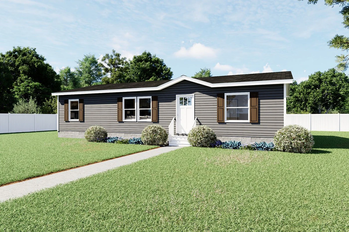 63678d78-7d90-41bf-9501-0926eea56ab4 Single-story gray manufactured home with white trim, brown shutters, small front steps, shrubs, and a concrete walkway, set on a grassy lawn with a white fence and trees in the background.