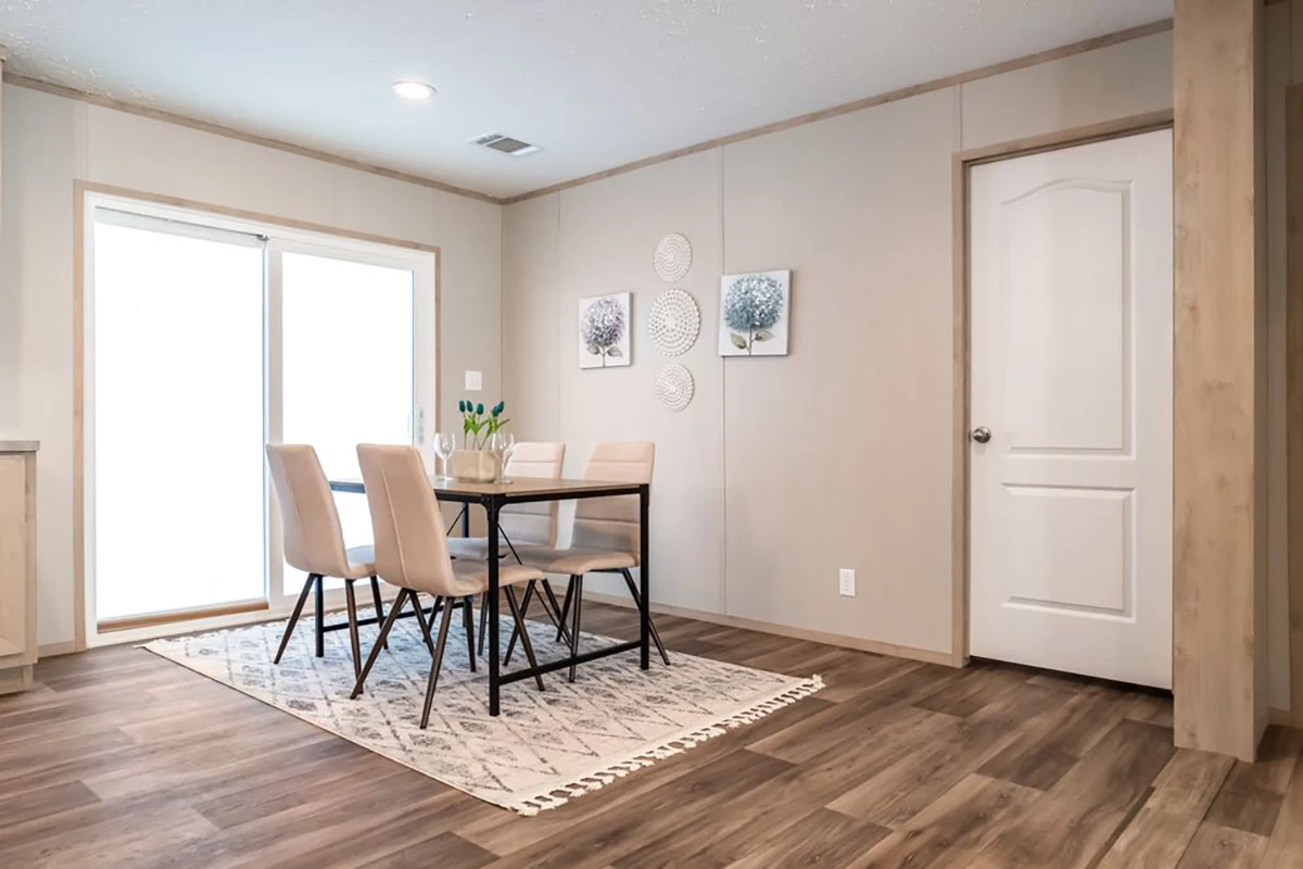 A modern dining area with a rectangular table, four chairs, a patterned rug, wall art, and large sliding glass doors, set on wood-look flooring.