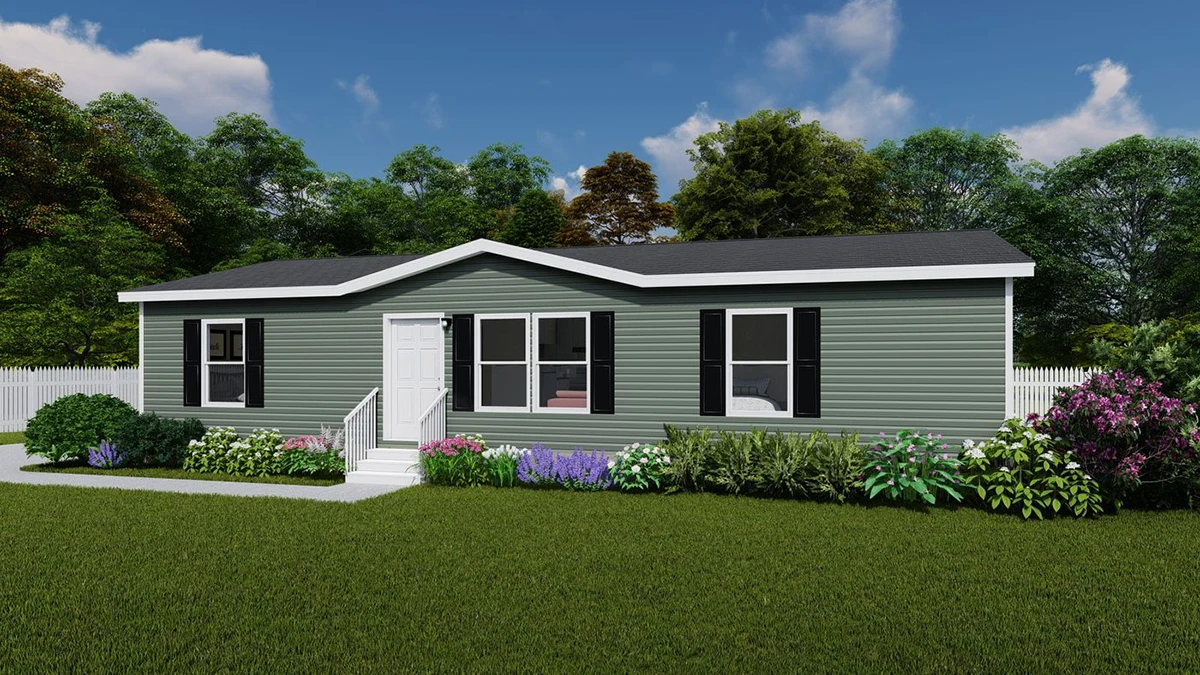 65f58c87-1c26-49f7-8d2a-789de47224cb Single-story manufactured home with green siding, black shutters, and white trim, surrounded by shrubs and flowers, set in a grassy yard with a white fence and trees in the background.