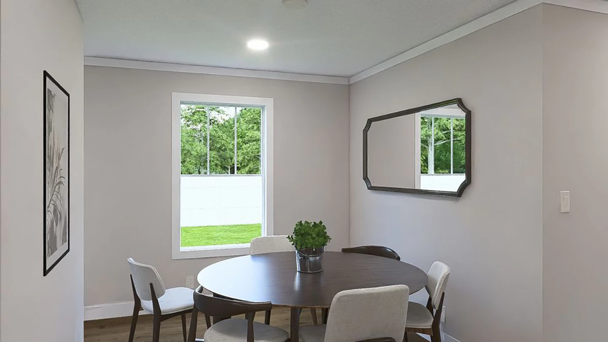 A small dining area with a round table, five chairs, a potted plant centerpiece, a wall mirror, a framed picture, and a window overlooking a green yard.