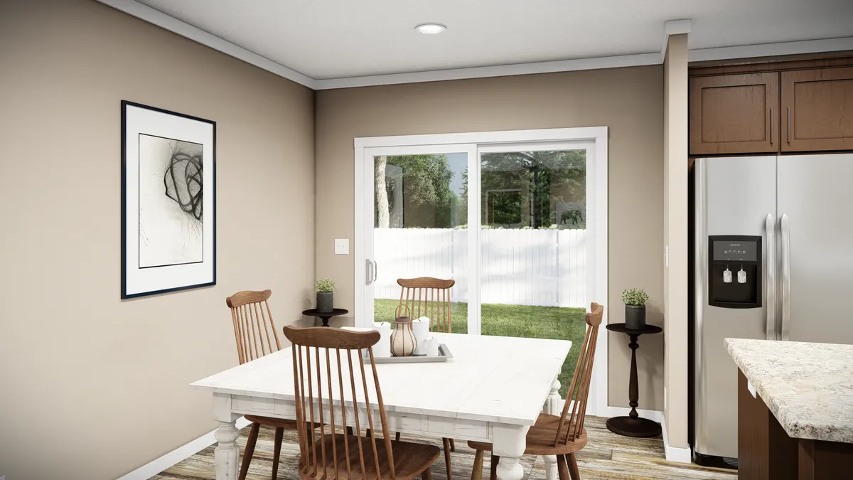 A small dining area with a white table and four wooden chairs, a framed abstract artwork on the wall, and sliding glass doors leading to a fenced backyard.