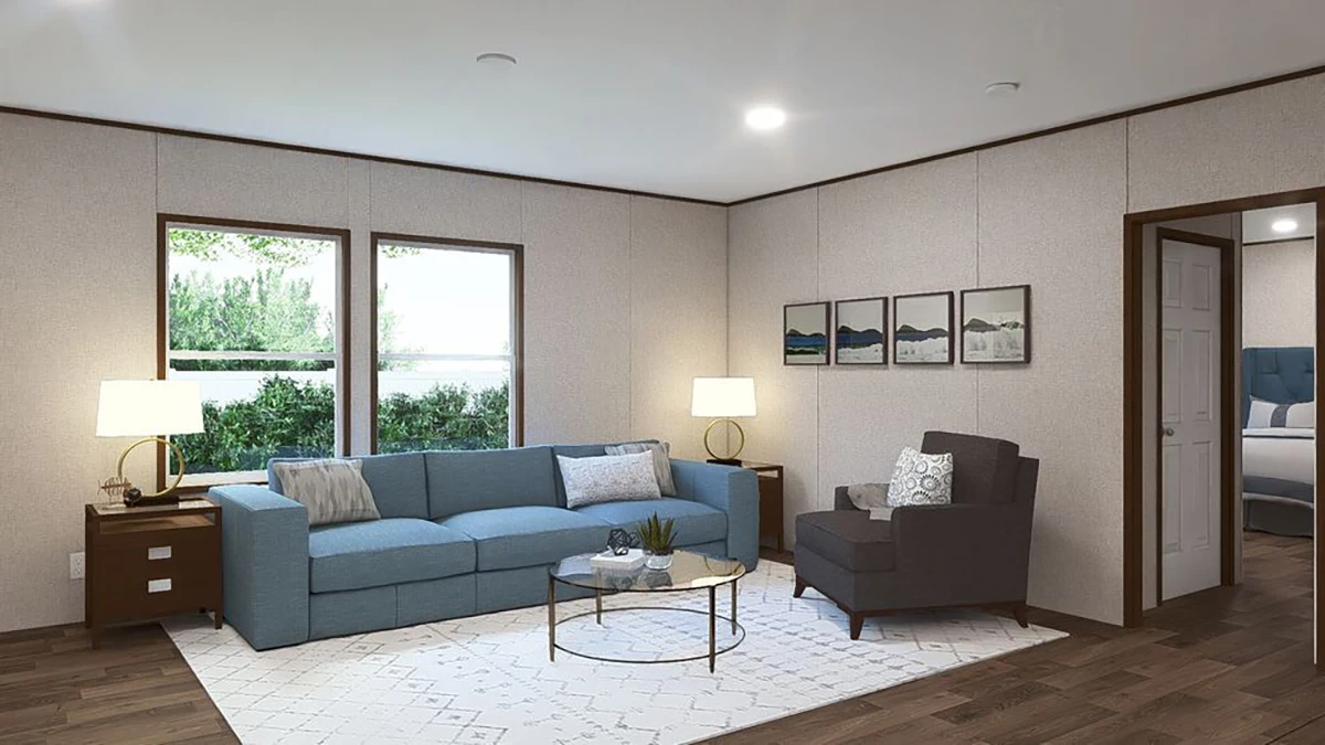 A living room with a blue sofa, gray armchair, round coffee table, two lamps on side tables, five wall art pieces, and large windows with a view of greenery.