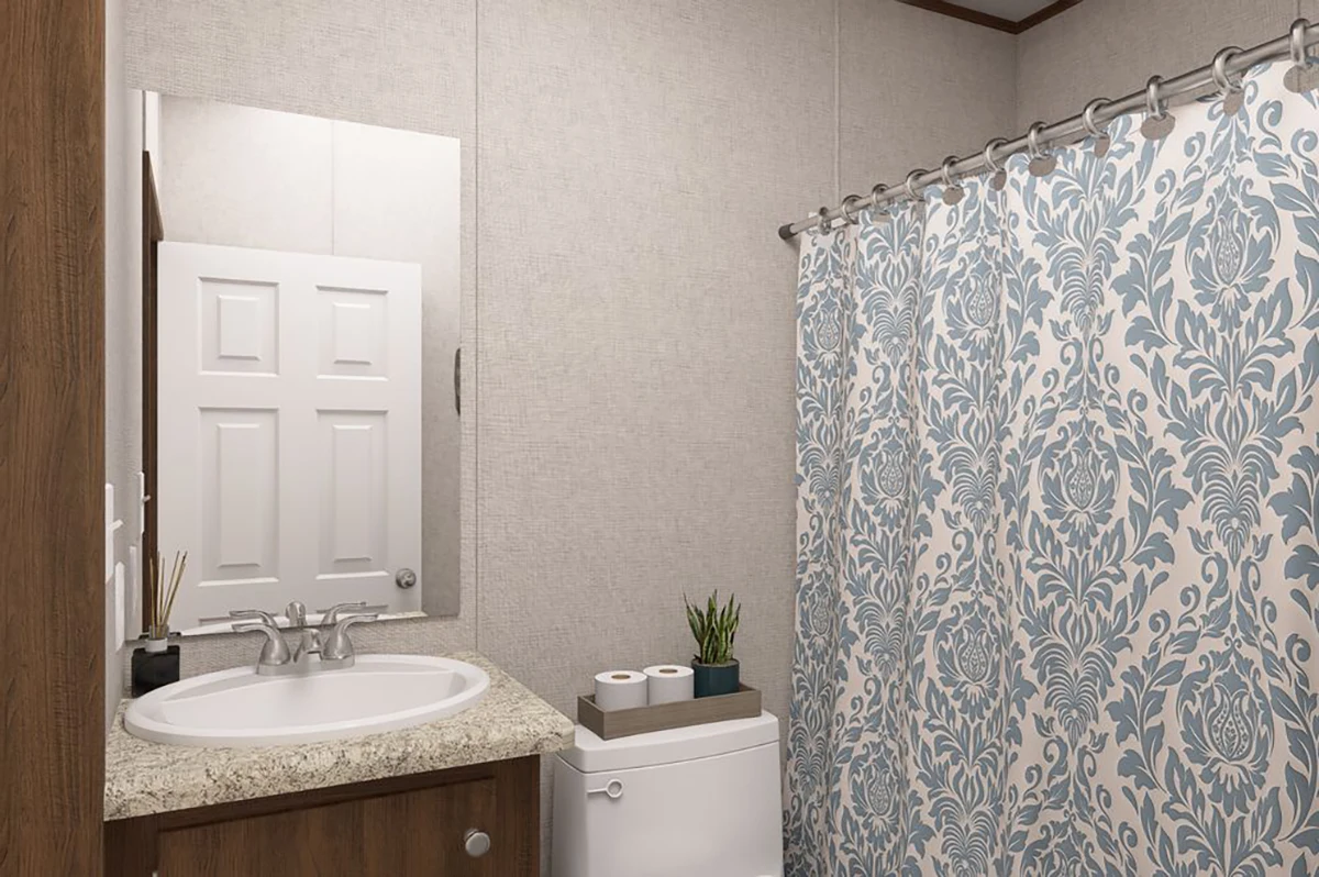 Bathroom with a sink and mirror, a toilet with toilet paper rolls and a plant on top, and a shower with a blue and white patterned curtain.