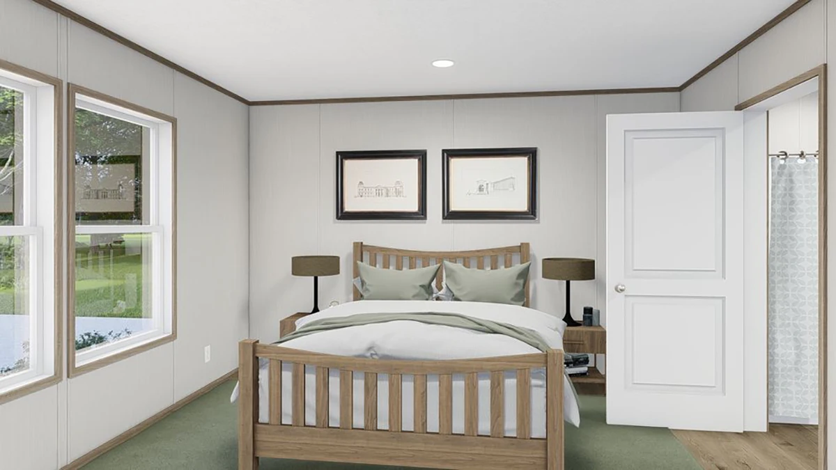 A bedroom with a wooden bed, two green pillows, matching nightstands with lamps, two framed pictures above the bed, and an open door showing a bathroom with a shower curtain.