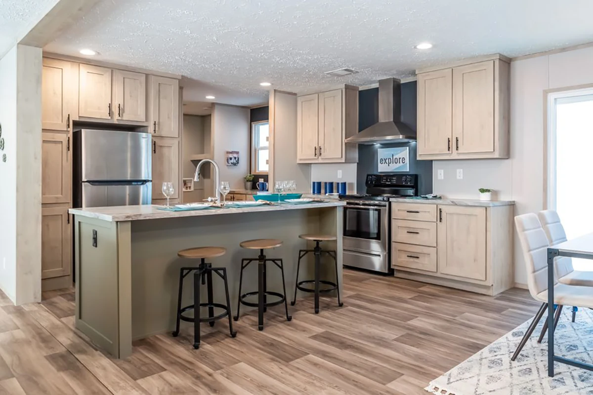 Modern kitchen with light wood cabinets, stainless steel appliances, a center island with three stools, and wood-look flooring. A dining table is partially visible on the right.