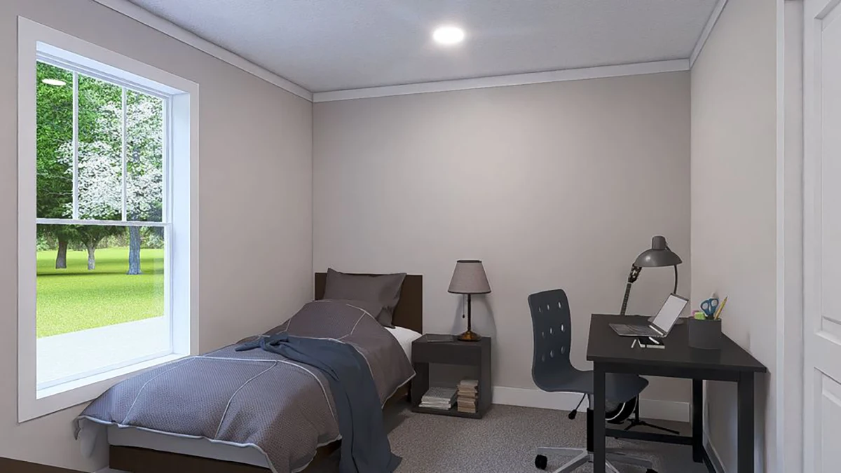 A small bedroom with a single bed, nightstand, lamp, books, and a desk with a chair, lamp, and laptop near a window showing a grassy outdoor view.