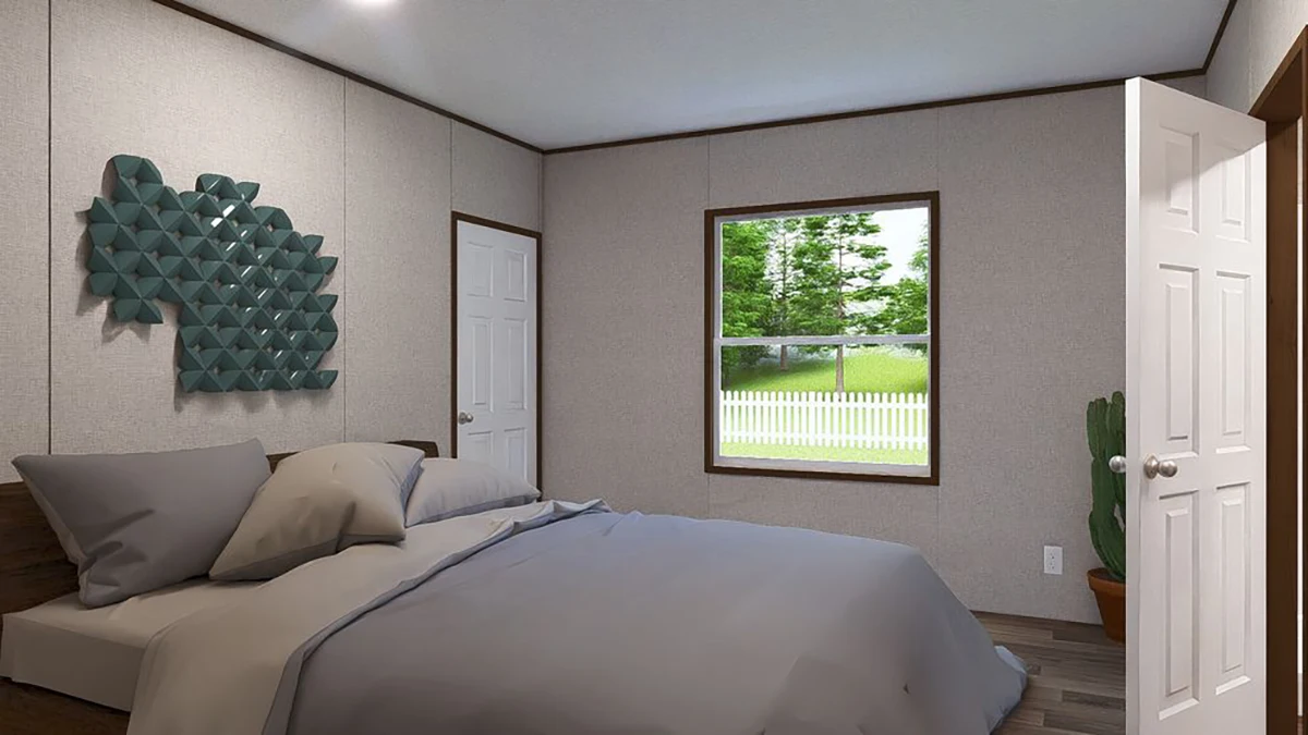 A neatly made bed with gray bedding is in a simple bedroom with a window, a closed door, wall art, and a potted cactus in the corner. Trees and a fence are visible outside.