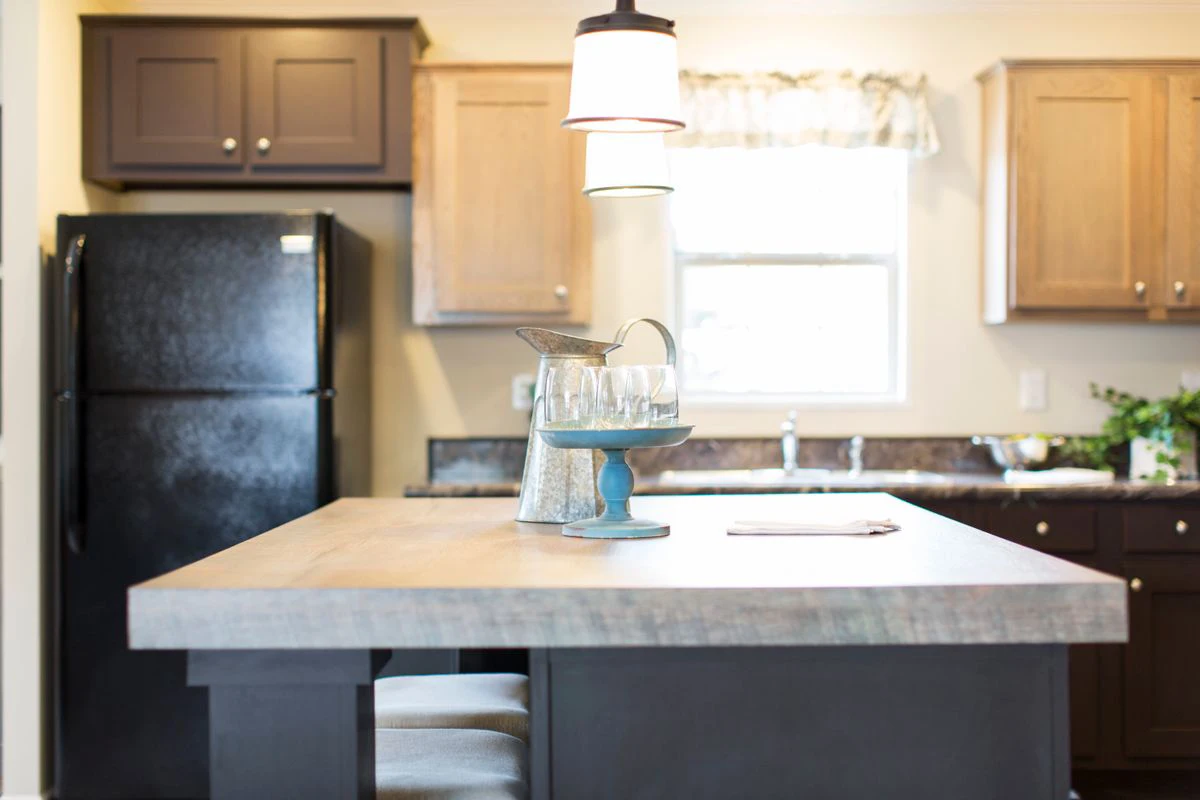 72bf8b2e-882c-4259-afc6-f0e8812175fe Modern kitchen with a wooden island, black refrigerator, upper cabinets, a window, and a tray with a pitcher and glasses on the counter.