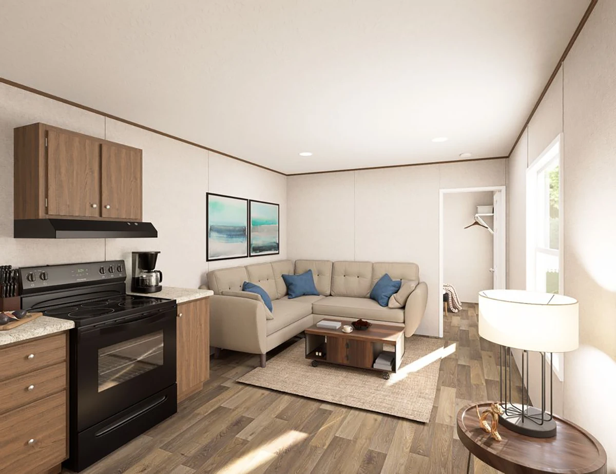 A compact living space features a kitchen with wooden cabinets and black appliances, a beige sectional sofa with blue pillows, coffee table, and a standing lamp on wood flooring.