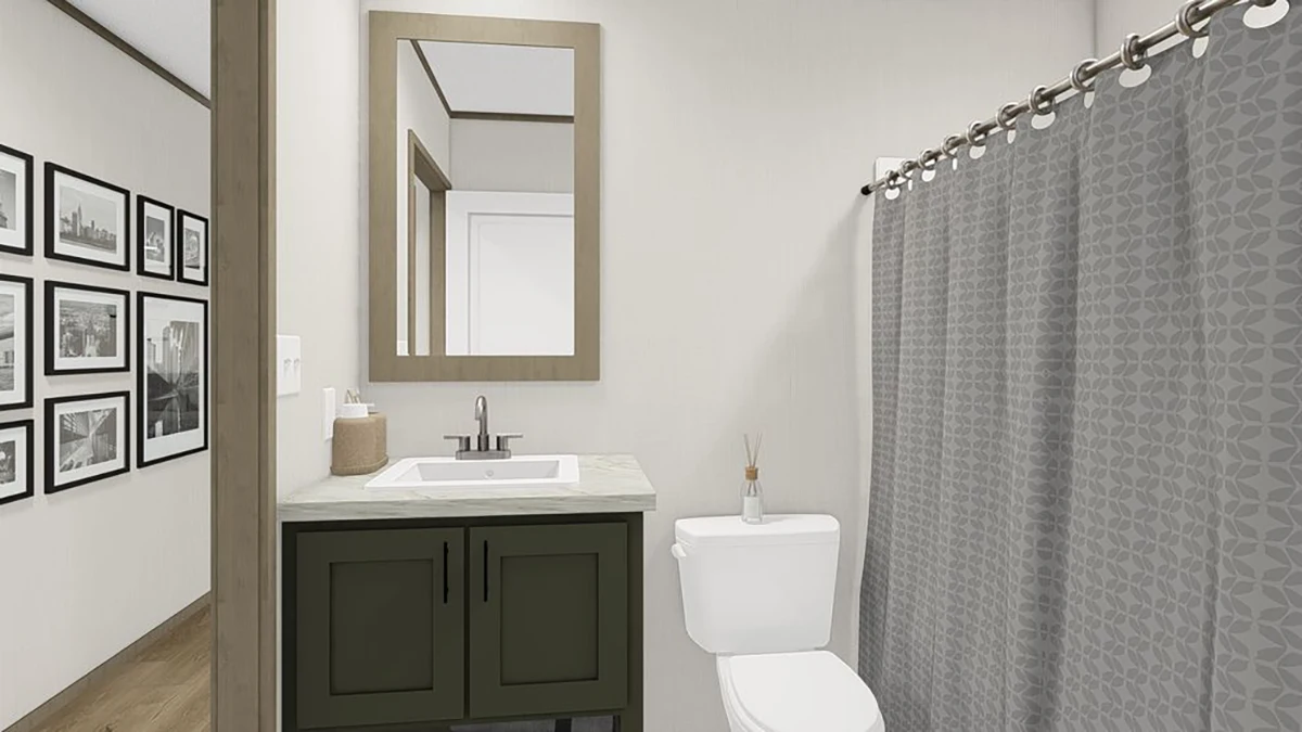 A modern bathroom with a sink and mirror, a toilet, a gray patterned shower curtain, and framed photos on the hallway wall outside.