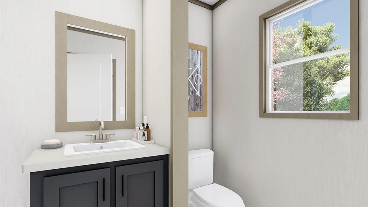 Modern bathroom with a sink and mirror on the left, a toilet on the right, a partial dividing wall, and a window showing greenery outside.