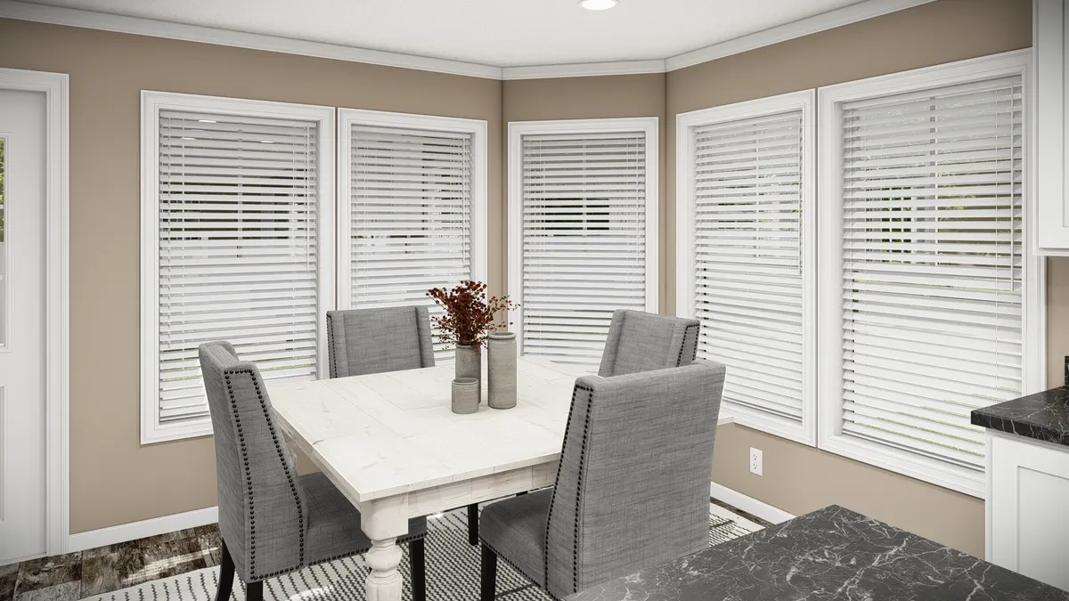 7c3c891e-94b8-4c1c-8975-0a9a27995bd4 A dining area with a white table, four gray upholstered chairs, beige walls, white blinds on windows, and a vase with dried flowers on the table.
