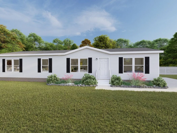 Single-story white manufactured home with black shutters, front lawn, small garden beds, and a driveway, set against a background of trees under a partly cloudy sky.