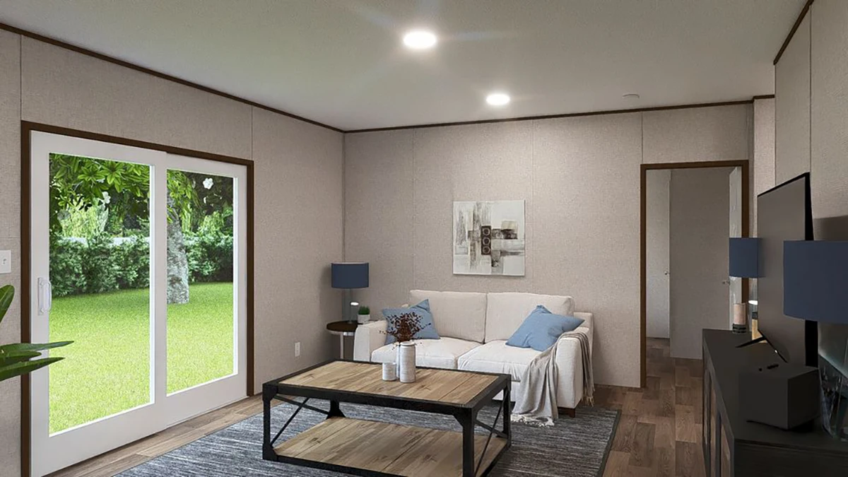 A modern living room with a white sofa, blue pillows, coffee table, rug, two lamps, wall art, TV and large glass doors overlooking a green backyard.