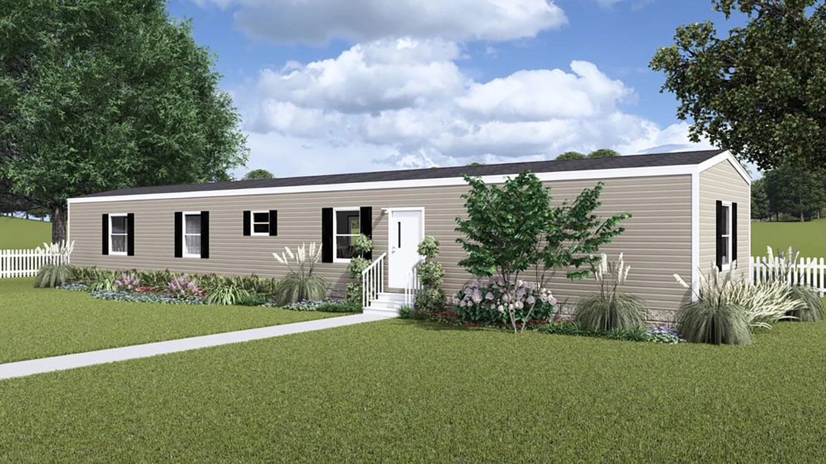 A beige single-wide manufactured home with white trim, surrounded by a lawn, landscaping, and a white picket fence under a partly cloudy sky.