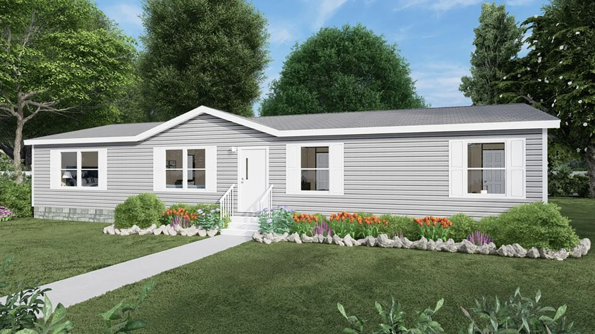 82bceba4-802d-417a-a716-b3164d000a15 Single-story gray manufactured home with white trim, front steps, and a landscaped garden with flowers and shrubs, surrounded by trees and grass under a blue sky.