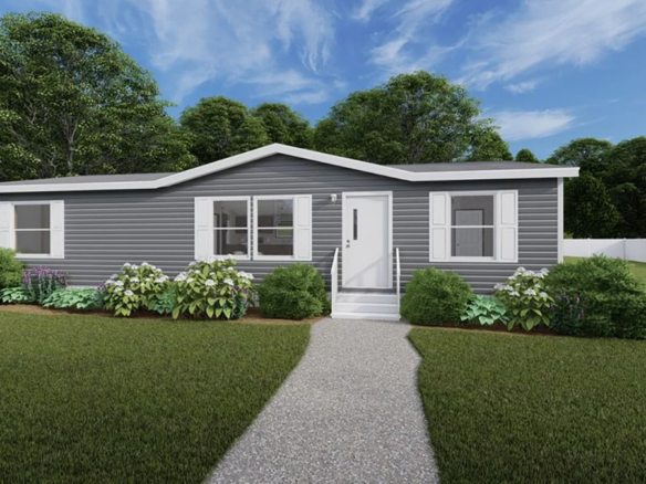A single-story gray manufactured home with white trim, white shutters, and a small front porch, surrounded by green bushes and a lawn, under a partly cloudy sky.