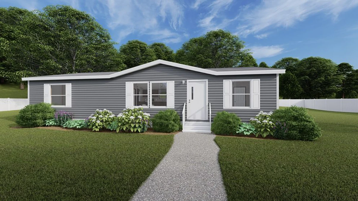 A single-story gray manufactured home with white trim, white shutters, and a small front porch, surrounded by green bushes and a lawn, under a partly cloudy sky.