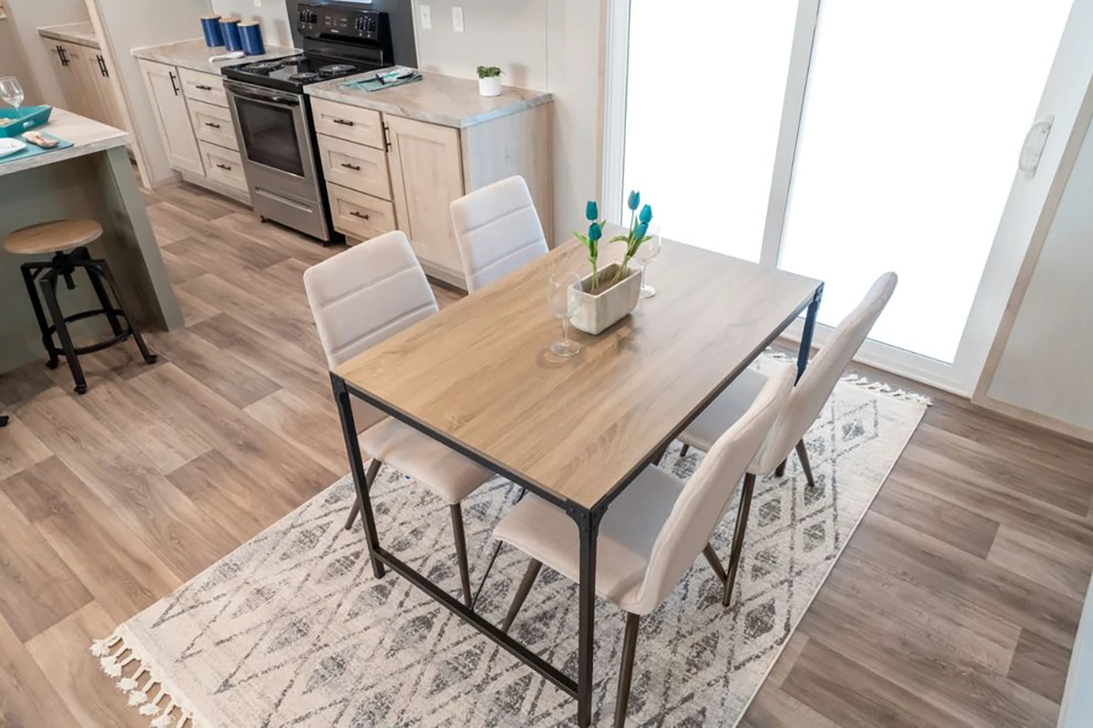 A modern kitchen and dining area with a wooden table, four upholstered chairs, a rug, and a stove in the background.