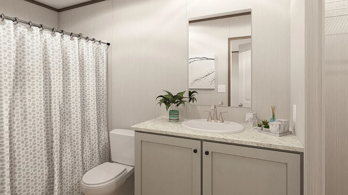 Modern bathroom with a shower curtain, toilet, and sink on a marble countertop with potted plant and toiletries, under a wall mirror.