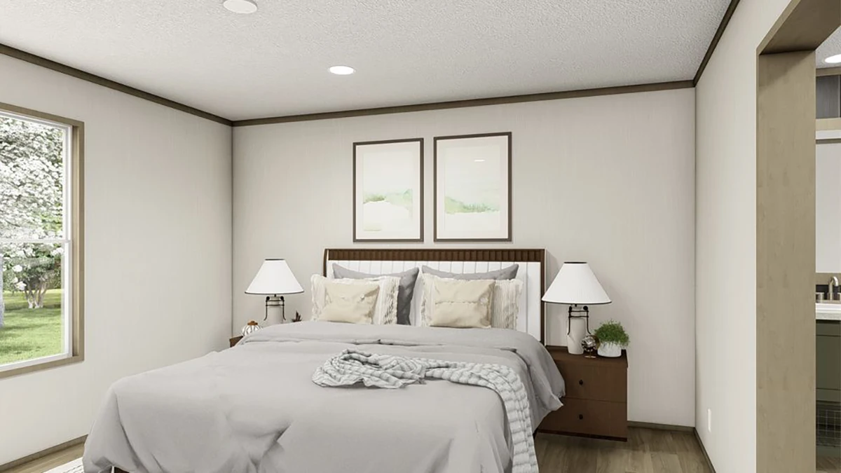 A neatly made bed with a blanket draped across it, two bedside tables with lamps, and two framed artworks above the headboard in a bright bedroom.