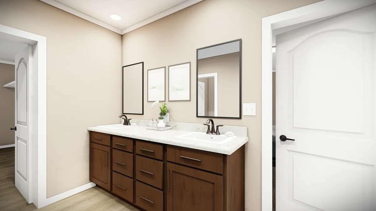 8b9c1c97-5d4b-4a2a-ac27-43f2276f583e Modern bathroom with double sinks, brown wood cabinets, two mirrors, framed wall art, and neutral-colored walls and doors.