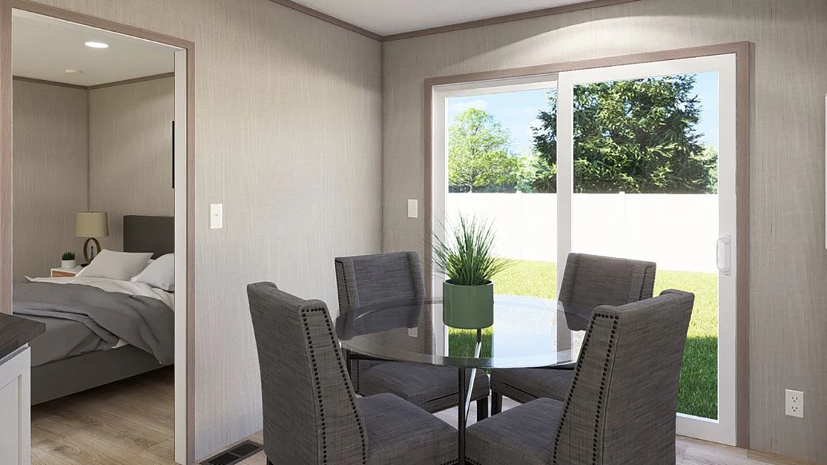 8eeff339-8925-40bd-8fe3-3481b7fc69c1 A small dining area with a round glass table and four gray chairs next to a sliding glass door, with a bedroom visible through an open doorway.