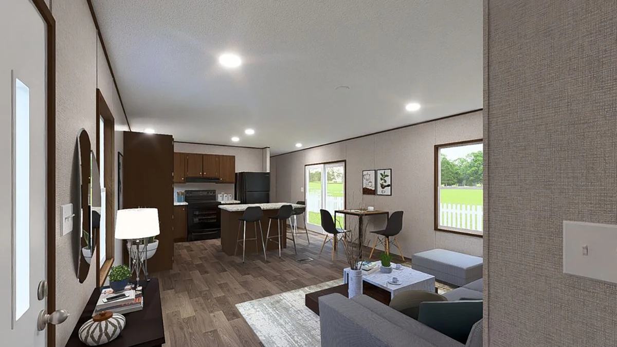 Modern open-concept living room and kitchen with wood floors, gray seating, dining table, and large windows overlooking a green yard and white fence.