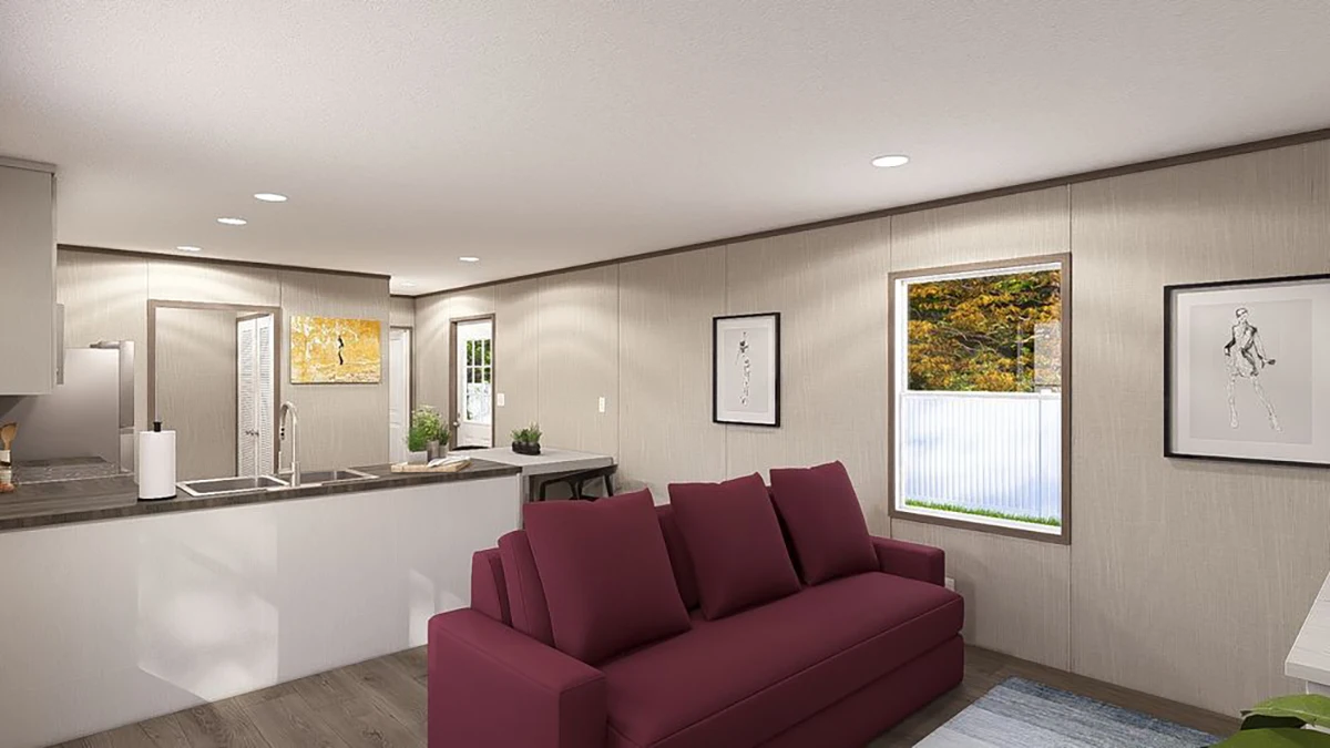 A modern living room and kitchen area with a maroon sofa, wall art, a window, and recessed lighting. The kitchen includes a sink island and countertop appliances.