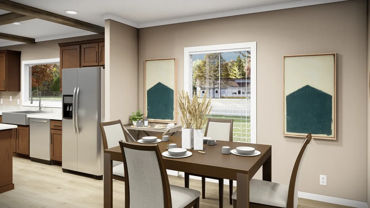 9731e4c0-7479-4553-9018-a053b1e06d0b A dining area with a rectangular table set for four, beige walls, modern art on either side of a window, and a stainless steel refrigerator visible in the adjoining kitchen.