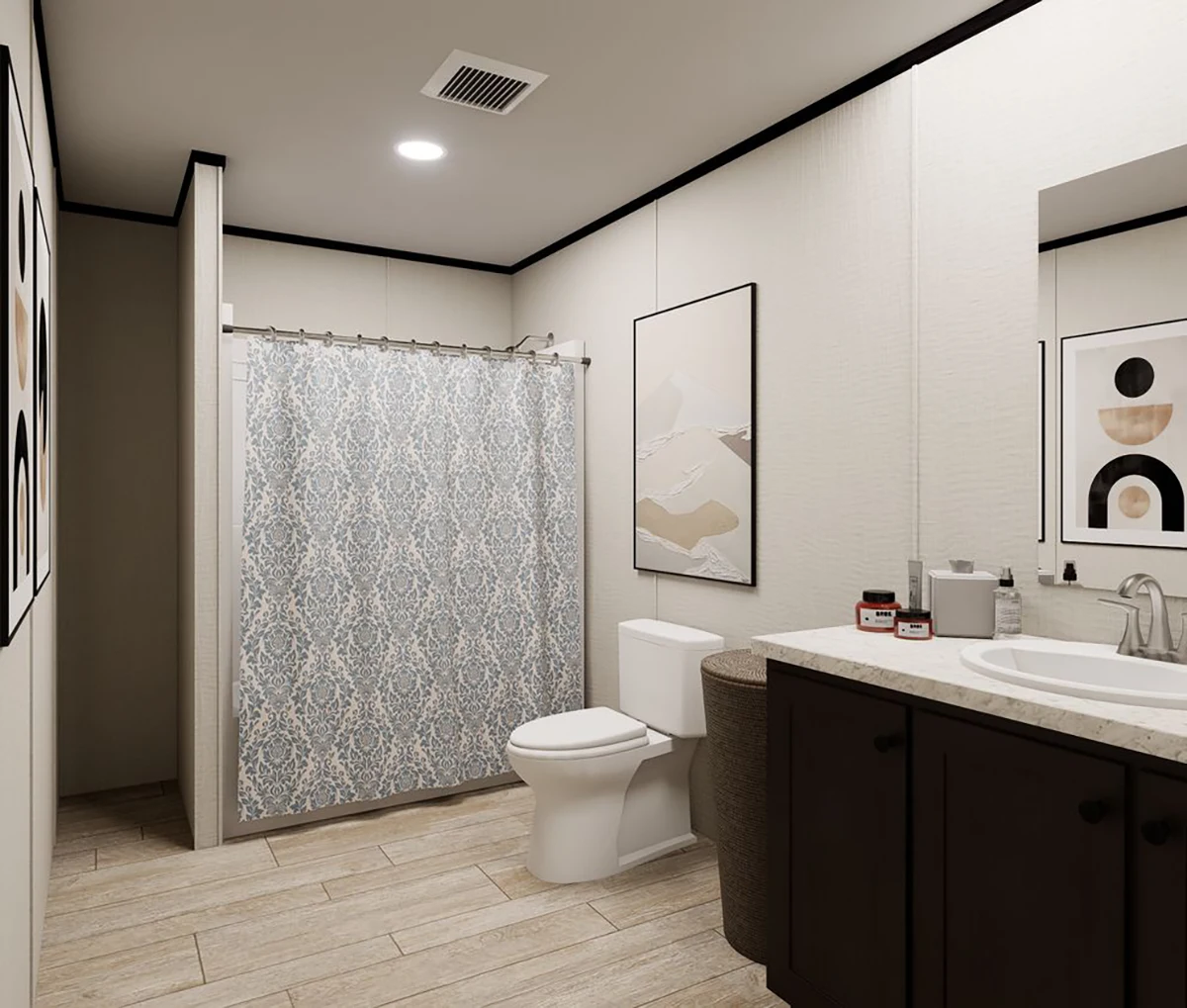 984738f9-a4fc-480a-9147-a26808efdf31 Modern bathroom with light wood floor, dark vanity, white sink, toilet, patterned shower curtain, and abstract art on the walls.