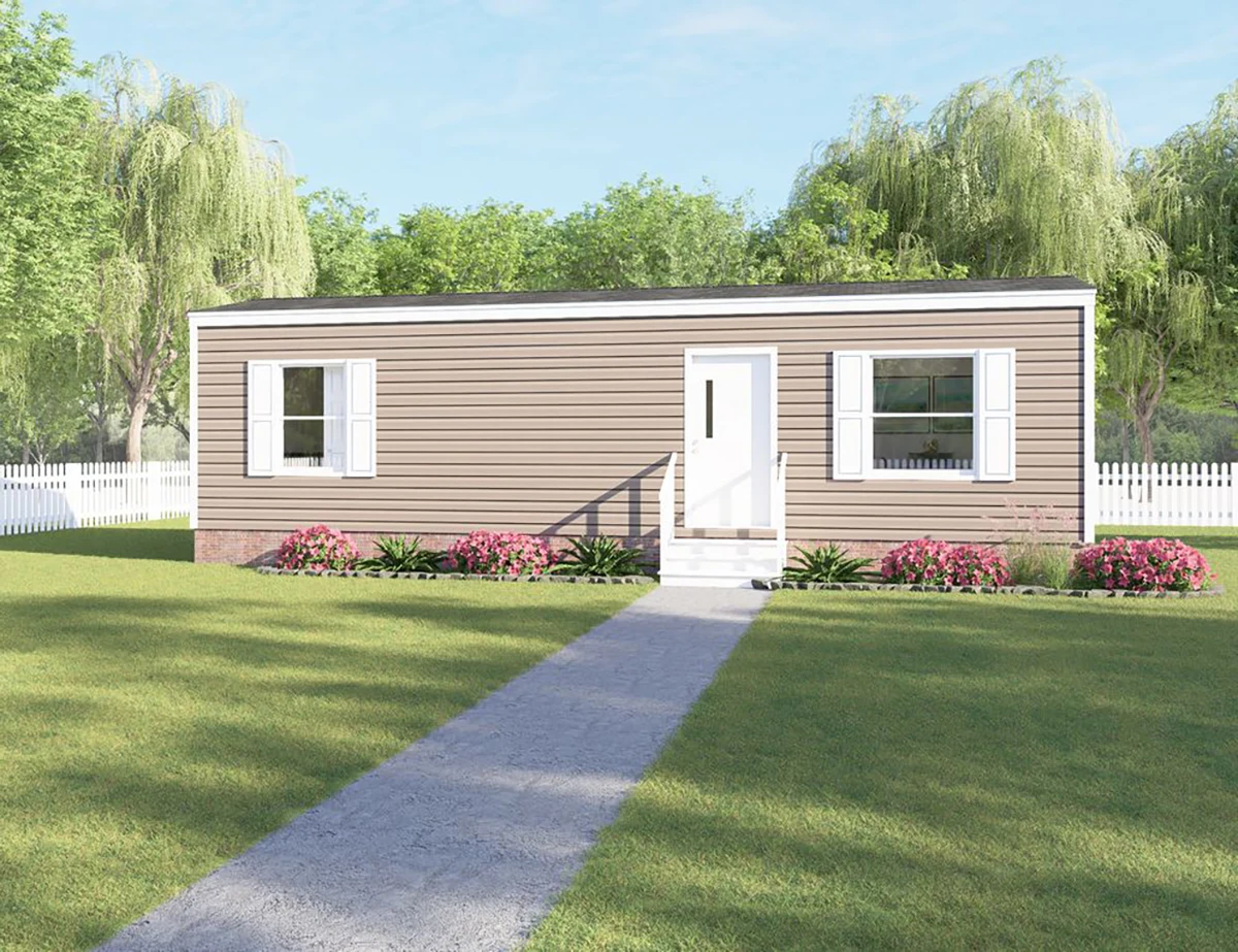 A single-story, beige manufactured home with white trim and shutters, front steps, and a path leading through a green lawn, surrounded by trees and a white picket fence.
