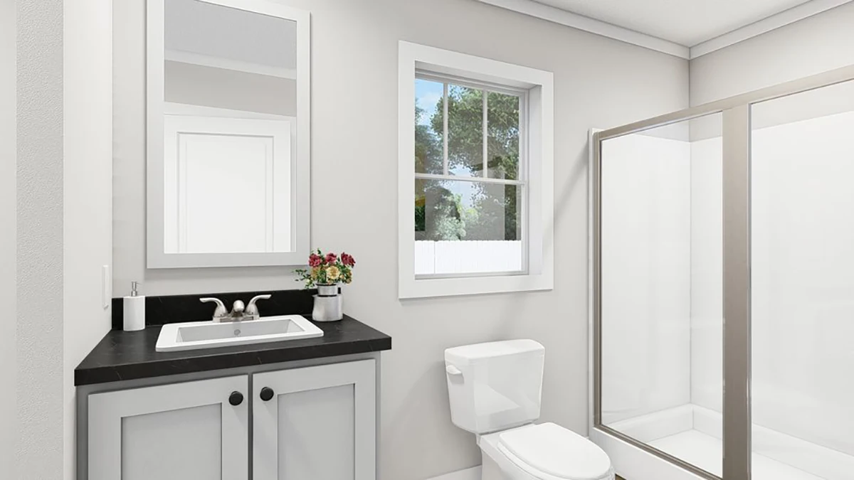 Modern bathroom with a white vanity and black countertop, a toilet, a glass shower enclosure, a wall mirror, a window, and a small vase with flowers on the counter.