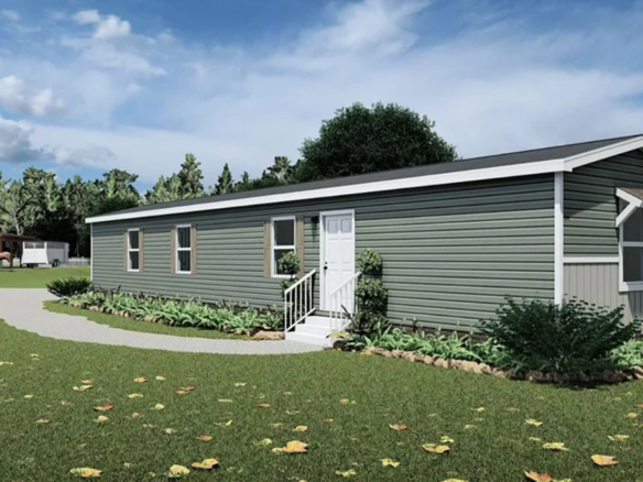 A green and white manufactured home with a small front porch sits on a grassy lawn with a curved walkway and landscaping, under a partly cloudy sky.