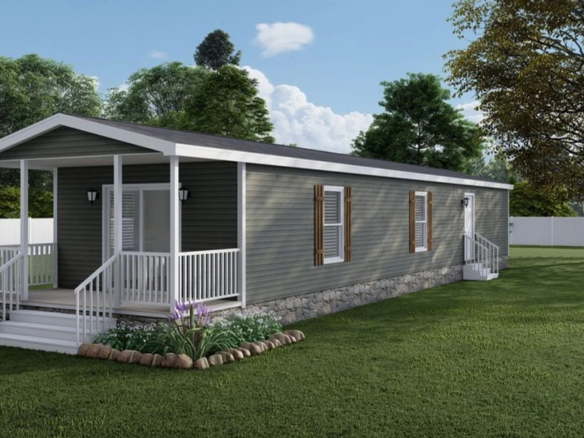 A single-story gray manufactured home with a small covered porch, white trim, and landscaped garden beds, set in a grassy yard with trees and a white fence.