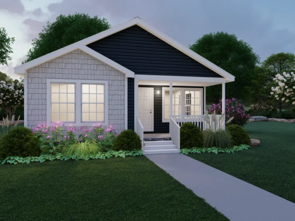 A small single-story house with a front porch, surrounded by lush green lawn, bushes, and flowering plants, with trees in the background at dusk.