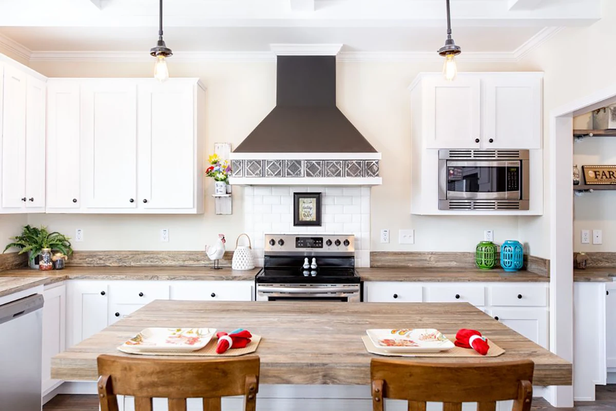 Modern kitchen with white cabinets, stainless steel appliances, wooden countertops, and a central island set for two with plates and napkins.