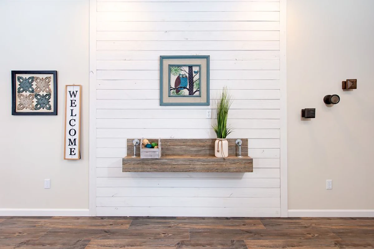 A minimalist entryway with a wood floating shelf, decorative vases, framed wall art, and a vertical "WELCOME" sign on a white shiplap wall.