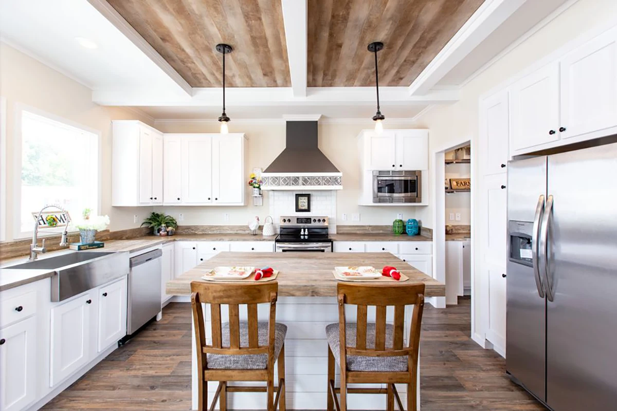 Southern Charm 10 Modern kitchen with white cabinets, stainless steel appliances, a wooden island with two chairs, and wood-accented ceilings.