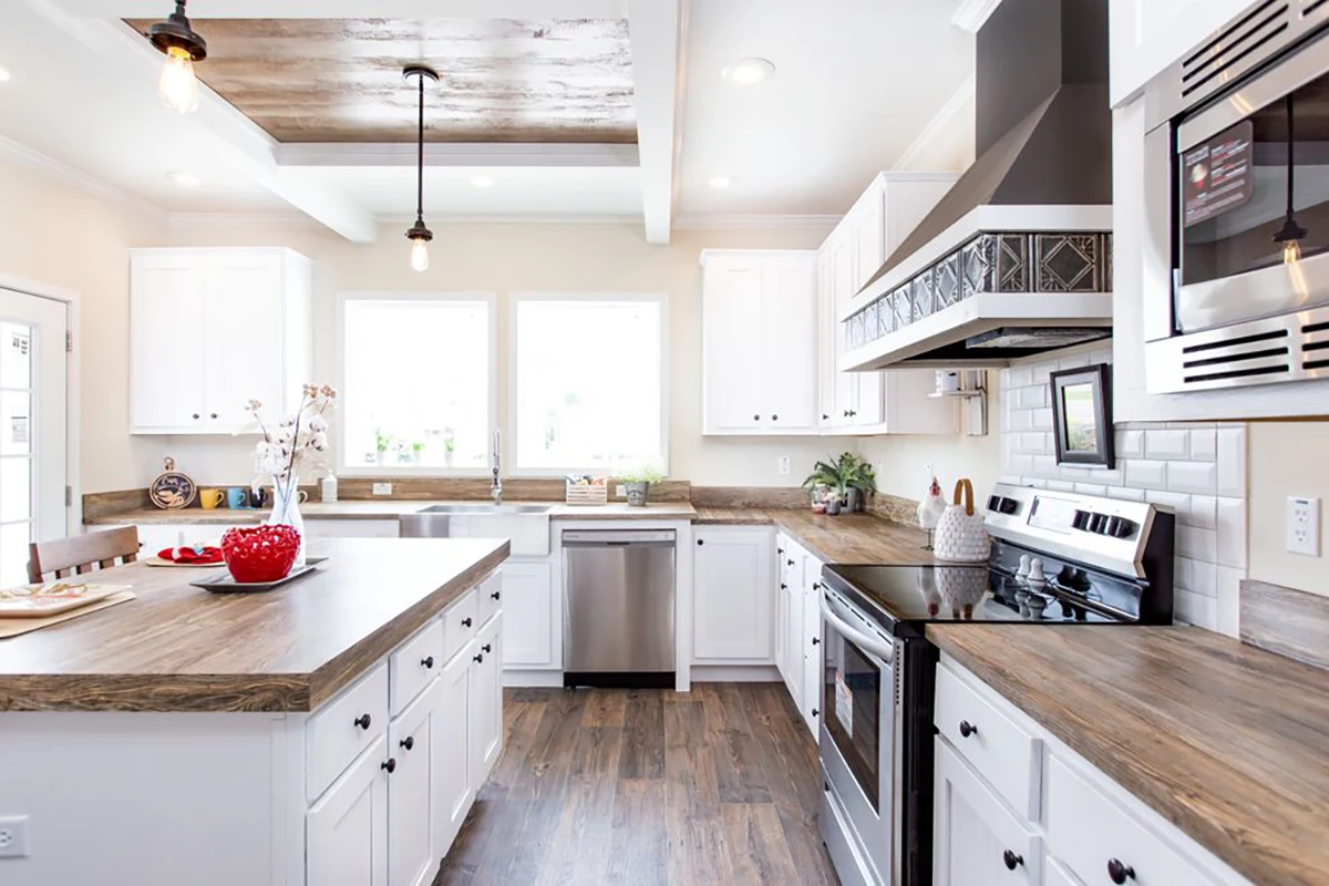 Southern Charm 11 Bright, modern kitchen with white cabinets, wood countertops, stainless steel appliances, and a center island with a bowl of red apples.