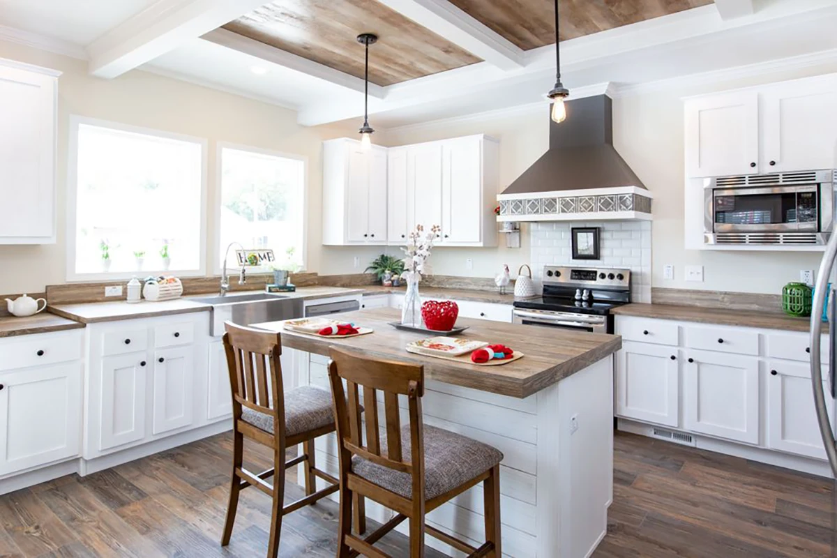 Southern Charm 4 Bright kitchen with white cabinets, wooden countertops, a central island with two chairs, stainless steel appliances, and pendant lighting.