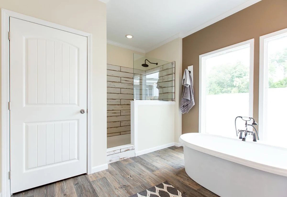 Southern Charm 5 Modern bathroom with a freestanding tub, walk-in shower with glass panel, towel hanging on the wall, large windows, and wood-look flooring.