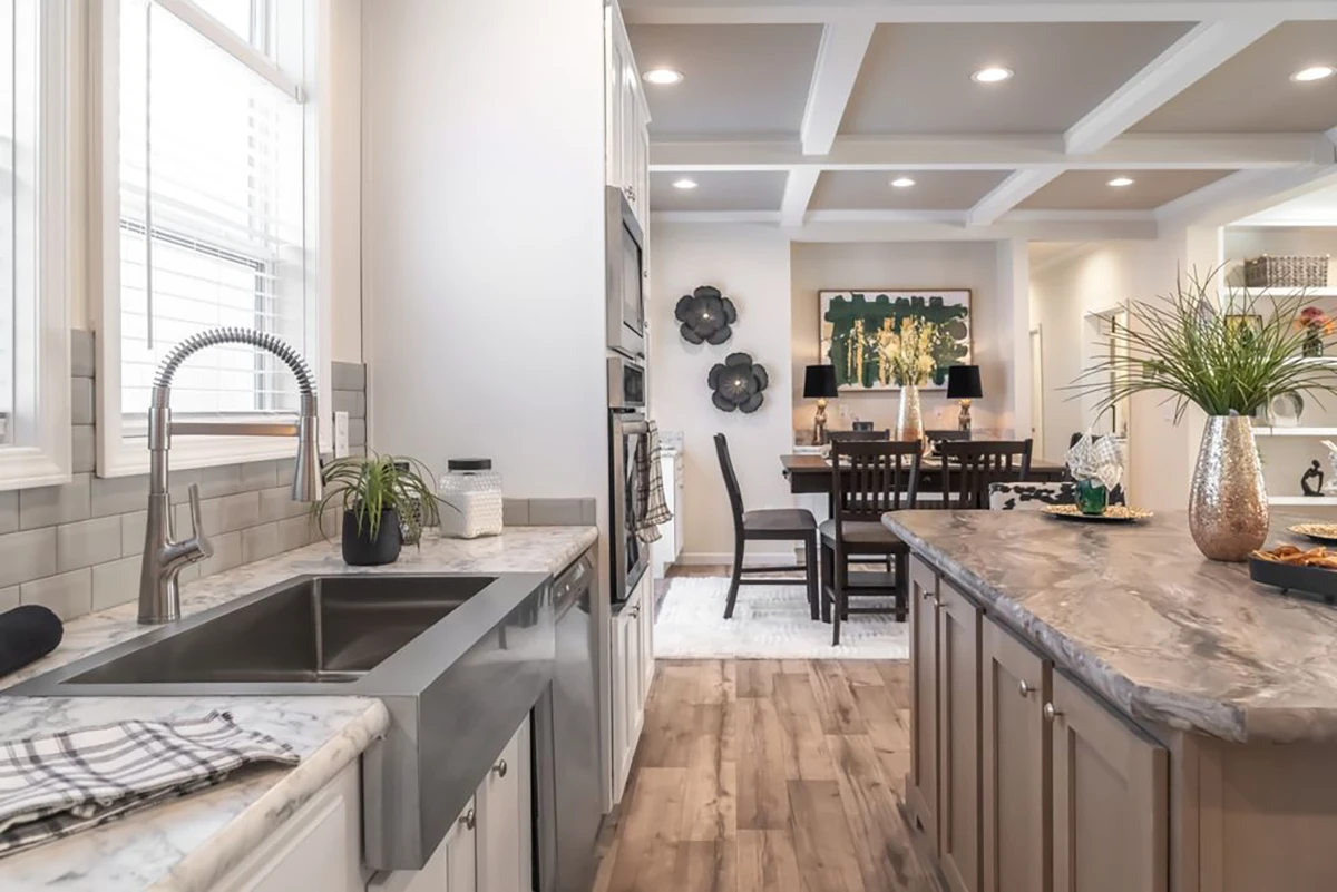 Modern kitchen with marble countertops, farmhouse sink, and stainless steel appliances, opening to a dining area with a wooden table and decorative wall art.