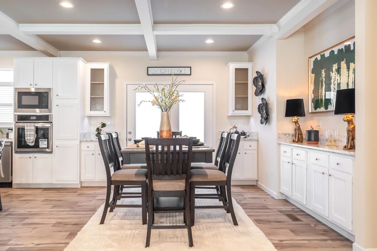 A modern kitchen and dining area with white cabinets, a wooden table with six chairs, decorative accents, and a vase with branches as the centerpiece.