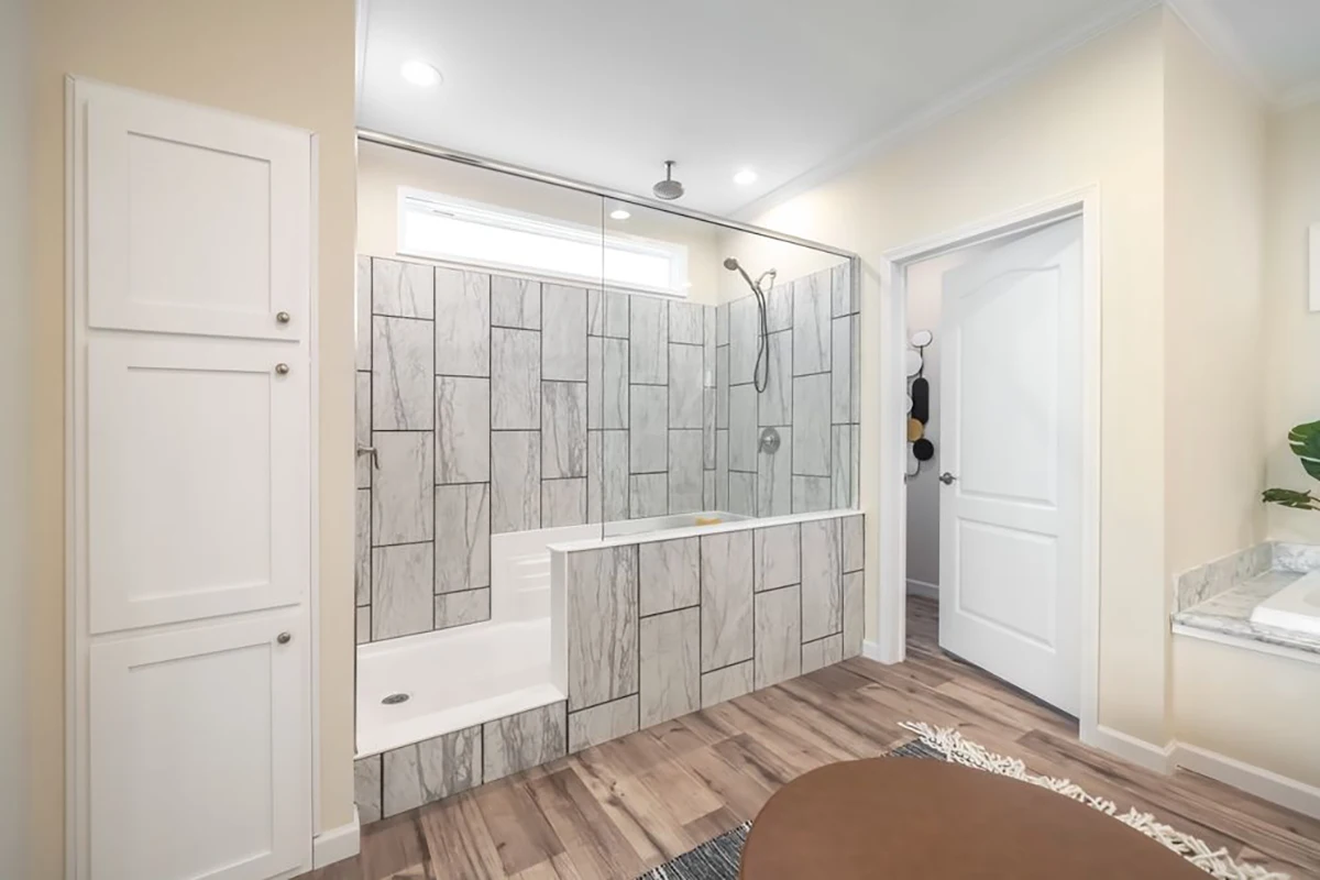 Modern bathroom with a walk-in shower and built-in bench, featuring gray tile walls, wood-look flooring, and white cabinetry.