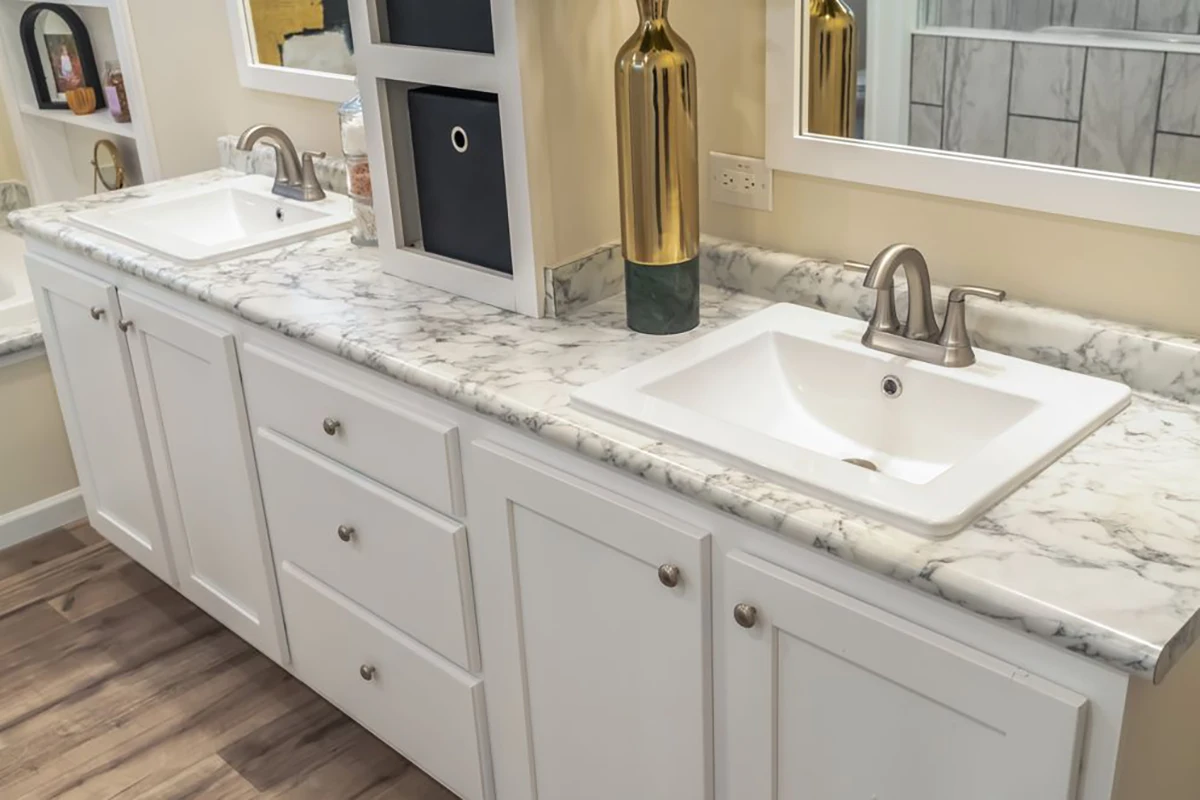 A bathroom vanity with a marble countertop, two square sinks, silver faucets, white cabinets, and decorative gold vases.