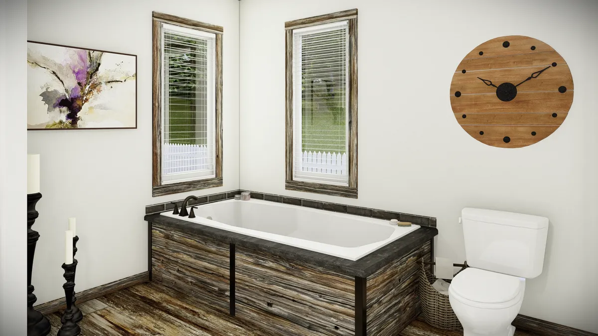 A bathroom with a wooden-framed bathtub, white toilet, two windows, wall clock, abstract painting, and wood-style flooring.