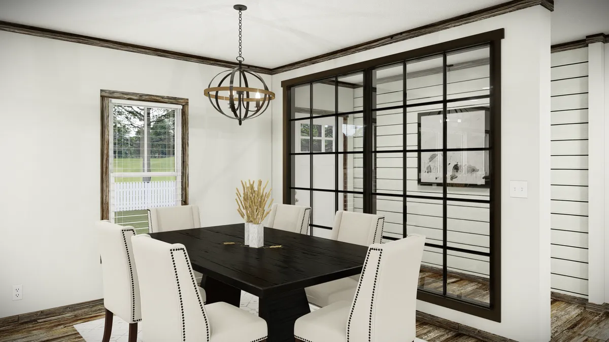 A modern dining room with a dark wood table, six white upholstered chairs, a geometric chandelier, and large black-framed windows overlooking a bright, grassy outdoor area.